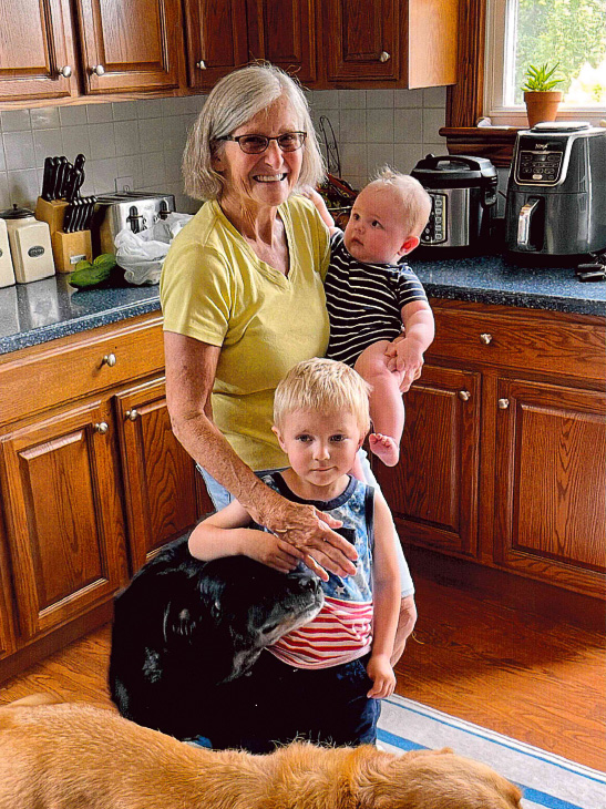 Donna is smiling with her grandchildren and two dogs in the kitchen.