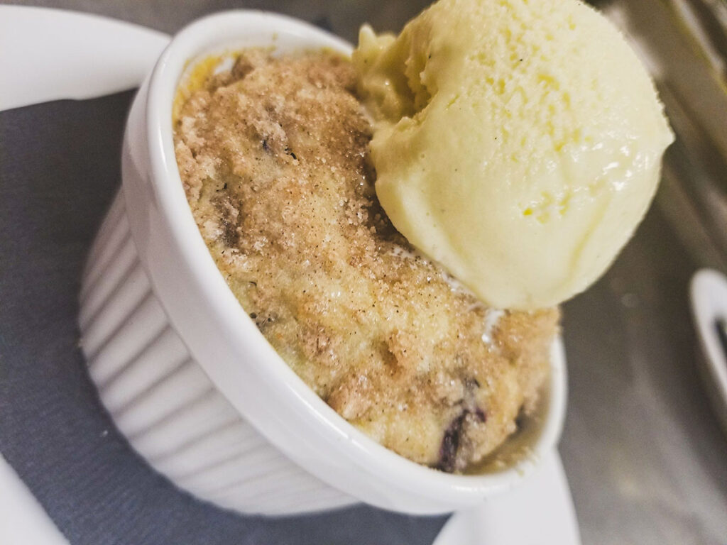 A delectable dessert in a bowl, featuring a scrumptious cobbler topped with a generous scoop of creamy ice cream.