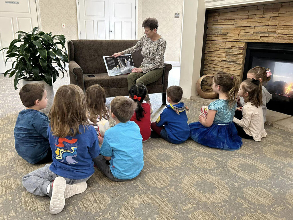 Celebrating Women's History Month, a senior resident captivates children's imaginations by reading "She Persisted" in front of a crackling fireplace. The Nest Schools Hudson joined the enlightening session!