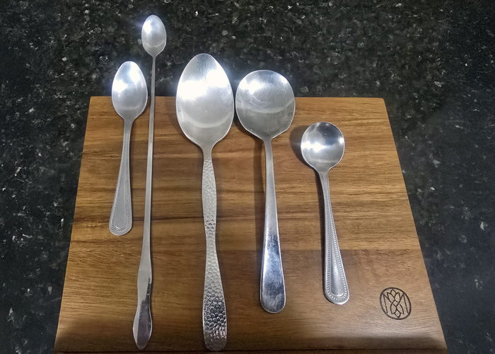 Five assorted silver spoons arranged on a wooden board, showcasing a range of sizes and styles ideal for kitchen tasks like plating, tasting, and prepping.